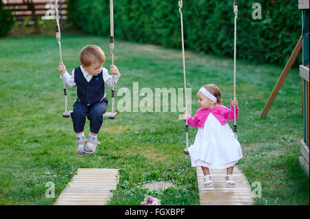 Petit garçon et fille monter sur une balançoire à l'aire de jeux dans le parc