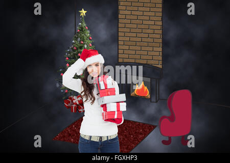 Composite image of brunnette in santa hat holding gifts Banque D'Images