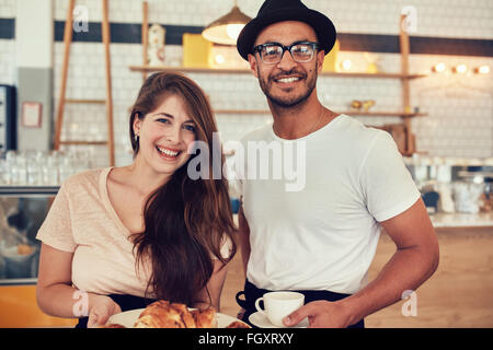 Portrait of happy young man and woman holding leur déjeuner dans un café à la caméra et au sourire. Couple avec des aliments et boissons à Banque D'Images