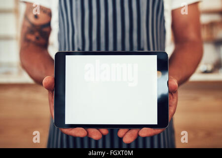 Portrait d'un homme portant un tablier, tenant une tablette numérique avec un écran blanc. Waiter holding un écran tactile ta Banque D'Images