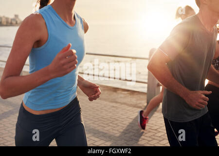 Cropped shot de jeunes le long de mer au coucher du soleil. Libre de droit du groupe de coureurs travaillant sur une route par la mer Banque D'Images