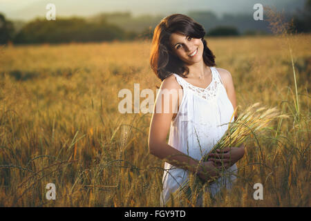 Belle femme dans un champ d'or au coucher du soleil. Portrait de la saison estivale Banque D'Images