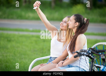 Voir le profil de deux happy smiling teenage girls wearing casual clothes sitting on park bench sur journée d'été Banque D'Images