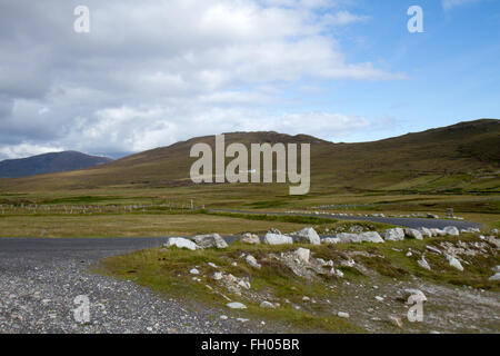 Des pierres sur le côté d'une route de montagne sur l'île d'Achill, Comté de Mayo, Irlande fr sous un ciel nuageux avec de vertes collines en arrière-plan Banque D'Images