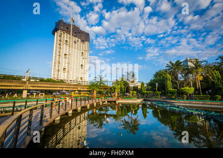 Skyscraper et promenade le long d'un étang à Rizal Park, à Manille, aux Philippines. Banque D'Images