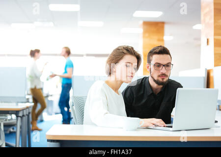 L'accent grave jeune homme et femme assise et travailler avec laptop in office Banque D'Images