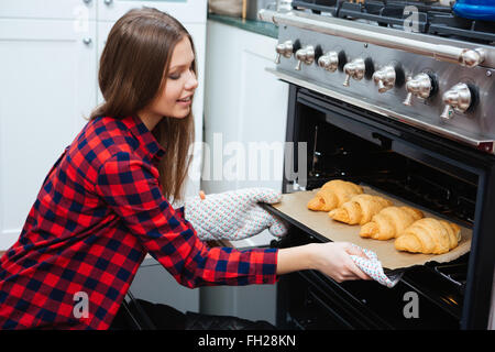 Smiling attractive young woman taking plateau avec des croissants du four sur la cuisine à la maison Banque D'Images