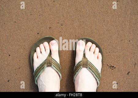 Regardant vers le bas sur les pieds d'un homme portant des tongs sur une plage de sable, Whitley Bay, Tyne & Wear, UK Banque D'Images