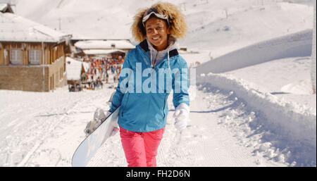 Smiling jolie jeune femme transportant un snowboard Banque D'Images