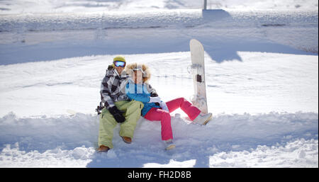 Happy young couple sitting on a plate-forme profonde de la neige Banque D'Images