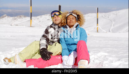 Couple assis dans la neige sur la pente de ski Banque D'Images