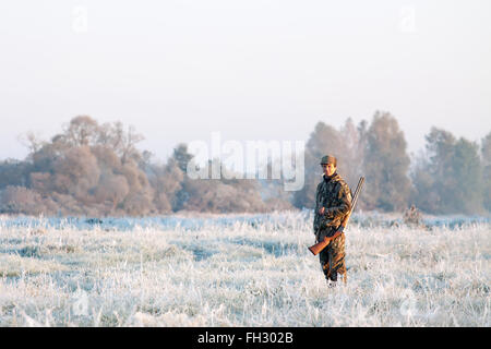 Hunter de camouflage avec un fusil sur son épaule en hiver sur un paysage gelé Banque D'Images