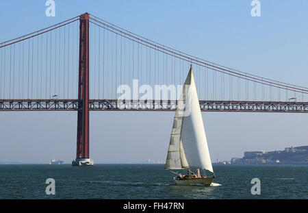 Lisbonne, Portugal. 14 Décembre, 2015. Un bateau à voile sur le Tage à l'avant de la Ponte 25 de Abril Bridge à Lisbonne, Portugal, le 14 décembre 2015. Le pont est le deuxième plus long pont suspendu, après le Pont de Tsing Ma à Hong Kong, et assure les trafics ferroviaire et routier. Photo : Hauke Schroeder/dpa/Alamy Live News Banque D'Images