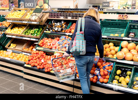 Une femme qui fait ses courses de fruits et d'autres produits d'épicerie dans l'allée du supermarché Tesco, Suffolk, Royaume-Uni Banque D'Images