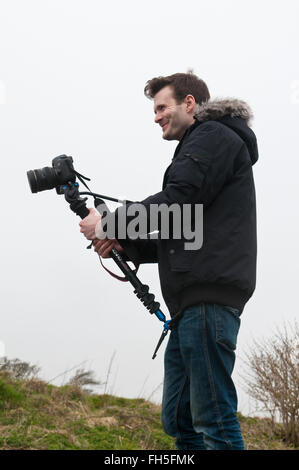 Jeune homme portant un manteau de style parka noire à l'aide d'un Canon EOS 5D DSLR avec un caméscope, un appareil photo Banque D'Images