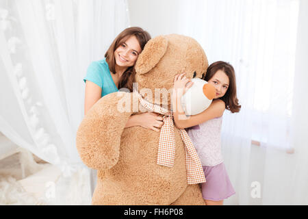 Deux belles filles heureuse et embrassant permanent peluche énorme dans chambre enfants Banque D'Images