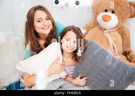 Portrait de deux belles soeurs sourire avec des oreillers jouant dans chambre enfants Banque D'Images