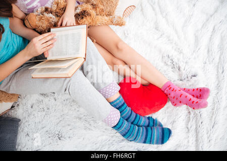 Libre de belles jambes de deux jeunes femmes en train de lire un livre sur le doux tapis Banque D'Images