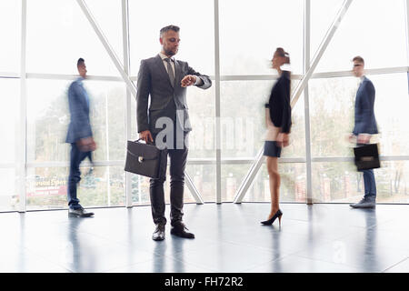 Serious businessman with briefcase looking at watch avec les gens pressés près de par Banque D'Images