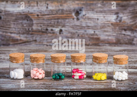 Divers comprimés et gélules dans des récipients en verre avec couvercles sur table en bois Banque D'Images