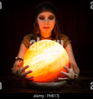 Jolie jeune femme Fortune Teller avec une boule de cristal, fond sombre Banque D'Images