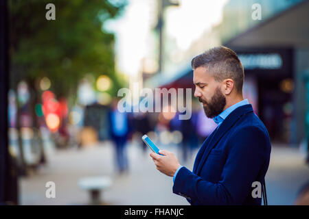 Hipster manager holding smartphone, l'envoi de messages texte à l'extérieur dans le stree Banque D'Images