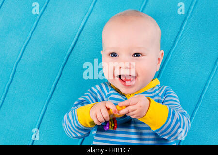 Mignon bébé tricoté bleu sur une couverture. La dentition à jouer avec des jouets colorés. Petit garçon au lit après pan. Banque D'Images