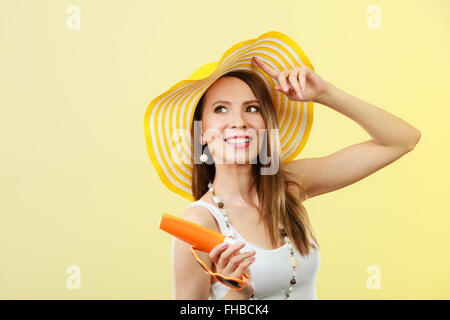 Vacances été la mode. et concept de soins de la peau. Femme au chapeau jaune en forme de cœur contient lotion solaire, lunettes arrière-plan lumineux copy space Banque D'Images