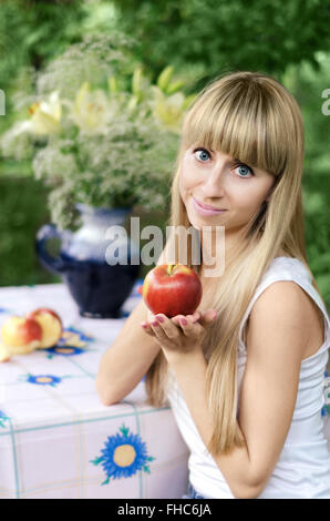 Girl holding Apple, assis à une table dans le jardin Banque D'Images