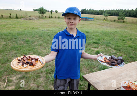 Garçon polonais de 12 ans contient jusqu'plateaux de kolbassa fraîchement cuisinés & boudin il cuit à l'extérieur grill Zawady Centre de la Pologne Banque D'Images