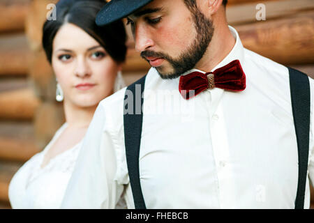 Groom réfléchie dans hat avec barbe, moustache, noeud papillon et des bretelles. Vêtu de blanc mariée robe de mariage. Style gangster. Banque D'Images