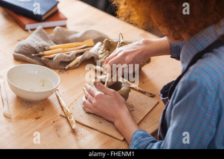 Curly concentré jeune femme travaillant sur pot en argile assis dans art studio Banque D'Images