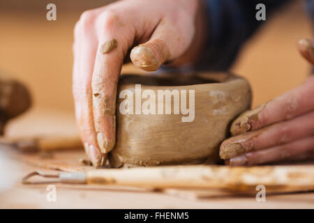 Gros plan du pot en terre par des mains de jeune femme potter sur table en bois en atelier Banque D'Images