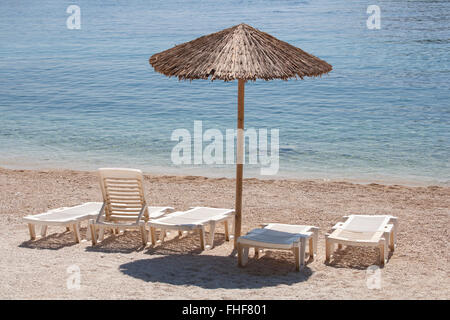 Parasol en bois avec plusieurs chaises longues sur une plage ensoleillée solitaire à l'eau claire. Banque D'Images