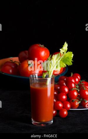 Hero shot d'un verre de jus de tomates d'une branche de céleri et les tomates sur une toile noire with copy space Banque D'Images