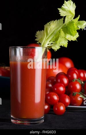 Hero shot d'un grand verre de jus de tomates d'une branche de céleri avec tomates fraîches et un fond noir Banque D'Images