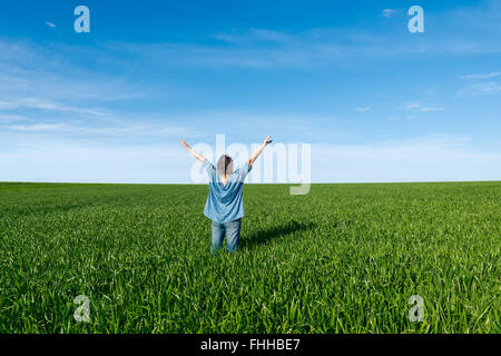 Femme avec les mains posées debout dos au champ vert contre le ciel bleu Banque D'Images