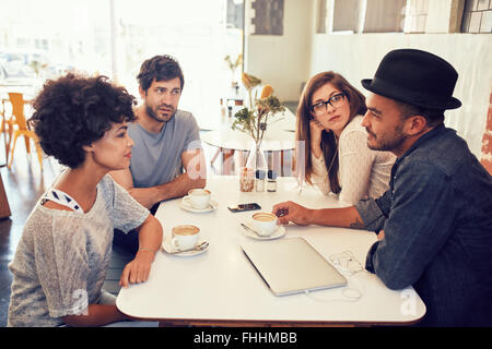 Portrait de jeunes hommes et femmes assis à une table de café et de parler. Groupe de jeunes réunion d'amis dans un café. Banque D'Images