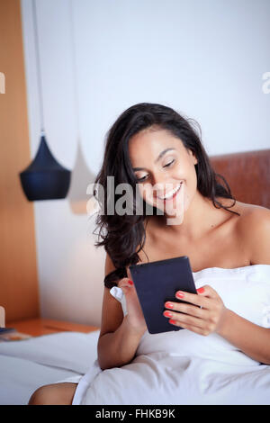 Hispanic woman en utilisant son appareil portable dans sa chambre d'hôtel Banque D'Images