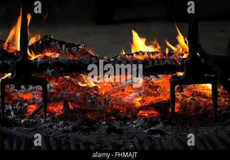 Bûches avec des flammes et des braises rougeoyantes dans immeuble ancien sur marbre en ouverture de grille cheminée centrale. Image chaud chaud confortable cheminée intérieure romantique. Banque D'Images