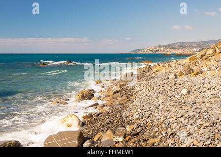 Les graviers de vagues se brisant sur l'eau, les cailloux et les rochers d'une plage vide dans la rude côte rocheuse de la Ligurie, au nord de l'Italie. Cl Banque D'Images