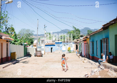 Dans un quartier pauvre de Trinidad à Cuba, une fille pousse son scooter en bas de la rue non pavée bordée de maisons aux couleurs Banque D'Images