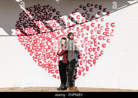 Jeune couple standing back to back en face d'un mur de briques avec un coeur Banque D'Images