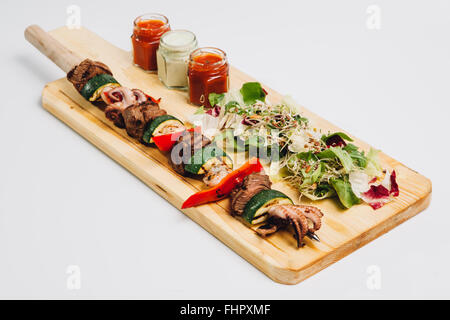 Stick avec des fruits de mer grillés, viande de boeuf, courgettes et paprik, sur la plaque en bois à côté d'une salade et de sources de Banque D'Images