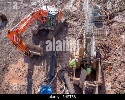 Digger et les travailleurs de la construction dans un trou de remplissage après la pose de nouvelles conduites d'égout Banque D'Images