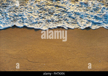 Belle lumière dorée qui brille sur la mer doucement glisser sur les vagues de la plage de sable. Banque D'Images