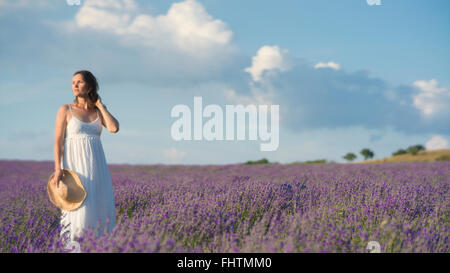 Belle jeune femme vêtue d'une robe blanche debout dans un milieu d'un champ de lavande en fleur. Banque D'Images