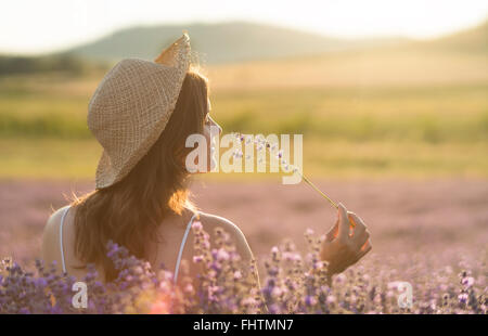 Belle jeune femme avec un chapeau de paille tenant un bouquet de fleurs de lavande et de profiter de leur parfum au milieu d'un laven Banque D'Images