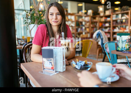 Belle femme parlant à un ami au restaurant tout en buvant du café Banque D'Images