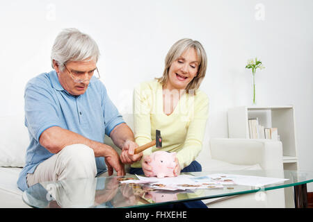 Senior couple casser tirelire avec un marteau à la maison Banque D'Images